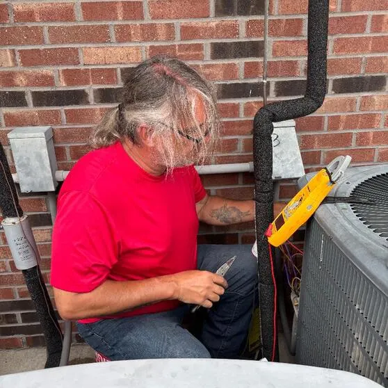 Technician performing high-precision electrical diagnostics and capacitor testing on an AC unit in Paxton, IL.